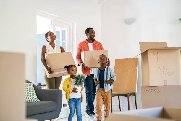 Black family with two children moving house Beautiful african american family with two children carrying boxes in a new home. Cheerful mature mother and mid adult father holding boxes while entering new home with son and daughter. Happy son and daughter helping parents relocating in new house with copy space. african american ethnicity stock pictures, royalty-free photos & images