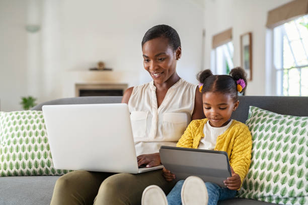 디지털 태블릿을 사용하는 딸 동안 집에서 일하는 여성 - laptop women child digital tablet 뉴스 사진 이미지