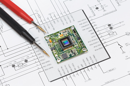 The module with the image sensor lies on the circuit diagram next to the tester probes. The concept of debugging, repairing electronic equipment