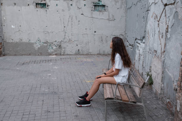 девочка-подросток сидит на скамейке между двумя обветренными стенами. горизонтальная композиция и пространство для копирования. - dirty grunge teenager relationship difficulties стоковые фото и изображения
