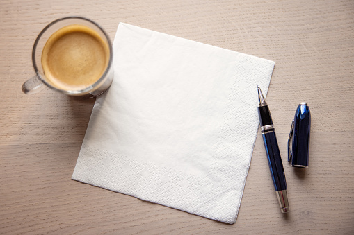White napkin on the table with cup of coffee and a pen. Concept of being creative anytime and anywhere
