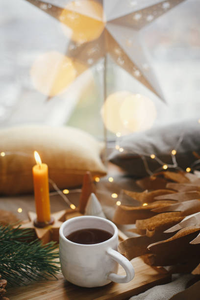 чашка чая, рождественская звезда, огни, деревья, свеча у окна. волшебный зимний хюгге. с рождеством - christmas window magic house стоковые фото и изображения