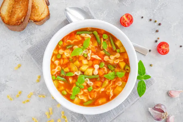 Minestrone soup of fresh vegetables and pasta in a bowl on a gray concrete background. Vegan dish. Copy space