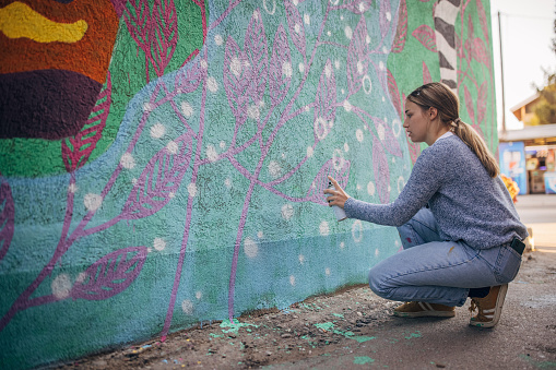 One woman, young female street artist spray painting on a building wall outdoors.