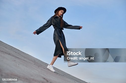 istock Beauty Fashion woman in black round hat and leather raincoat near lake pond. Portrait girl at sunset. Beautiful makeup and bright red lipstick on lips 1353385456