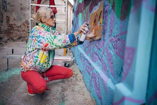 One woman, young female street artist spray painting on a building wall outdoors.