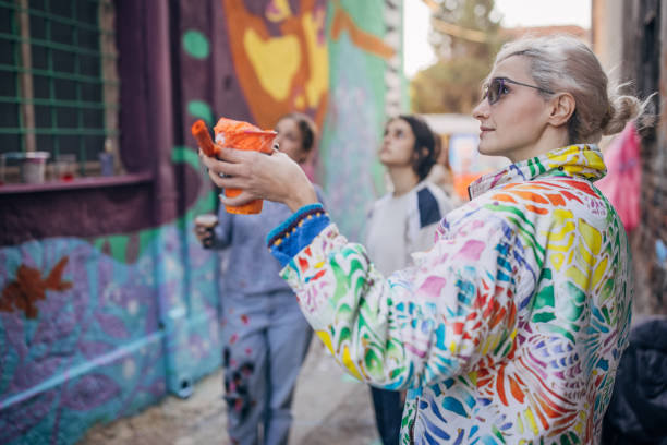 Three women, young females street artists looking together on a building wall drawing outdoors.