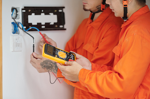 Hands of electricians using multimeter when fixing wiring in house and installing new multimeter