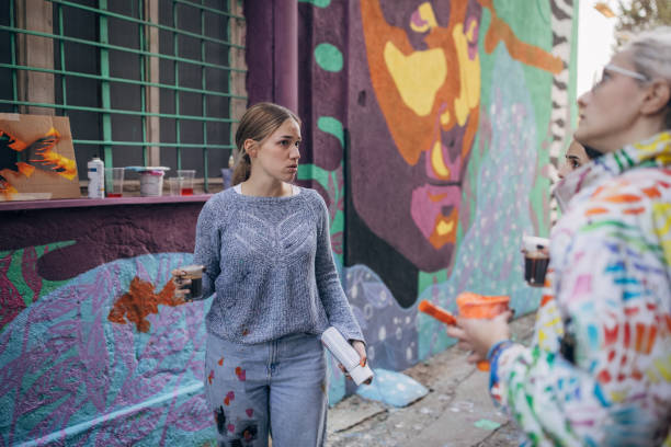 Three women, young females street artists looking together on a building wall drawing outdoors.