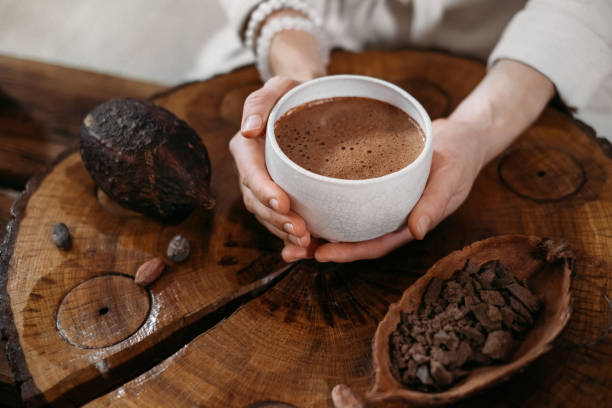 Person giving ceremonial cacao in cup. chocolate drink top view Hot handmade ceremonial cacao in white cup. Woman hands holding craft cocoa, top view on wooden table. Organic healthy chocolate drink prepared from beans, no sugar. Giving cup on ceremony, cozy cafe cacao fruit stock pictures, royalty-free photos & images