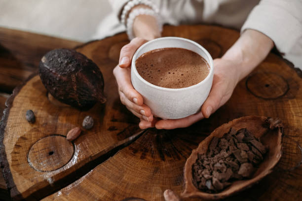 Person giving ceremonial cacao in cup. chocolate drink top view Hot handmade ceremonial cacao in white cup. Woman hands holding craft cocoa, top view on wooden table. Organic healthy chocolate drink prepared from beans, no sugar. Giving cup on ceremony, cozy cafe hot chocolate stock pictures, royalty-free photos & images