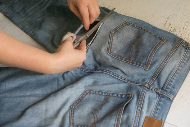 female hands with old torn jeans spread out on the table. the concept of clothing repair, recycling, home hobbies and work at home - manual worker sewing women tailor imagens e fotografias de stock
