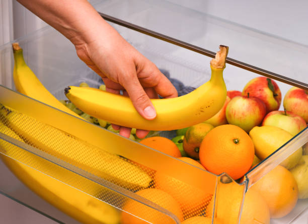 Woman taking banana from fridge drawer full of fruits stock photo