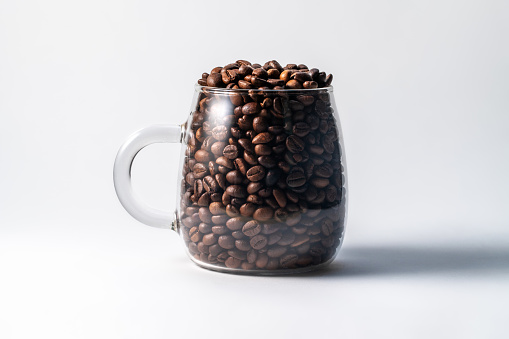 Glass mug full of coffee beans on white background