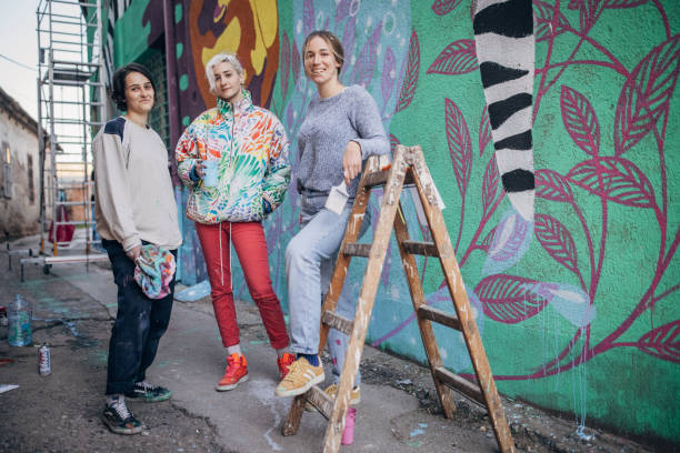 Female street artists Three women, young female street artists standing by a building wall drawing outdoors. street art mural stock pictures, royalty-free photos & images