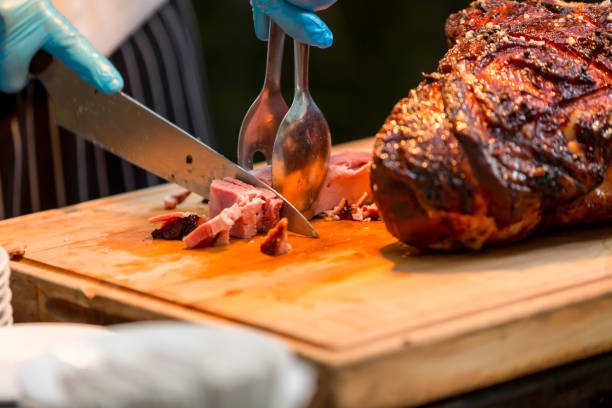 istock Grill restaurant kitchen. Chef in Blue cooking gloves using knife to cut smoked pork. Roast pork neck. Roasted shoulder of pork on a cutting board. 1353393609