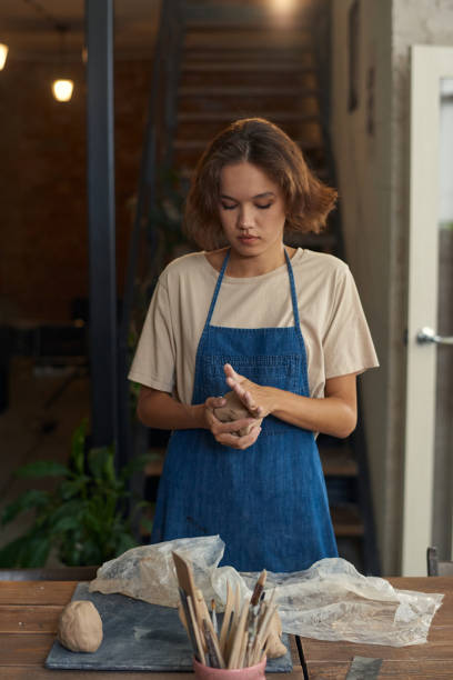 istock Young craftswoman kneading piece of clay between hands 1353393629