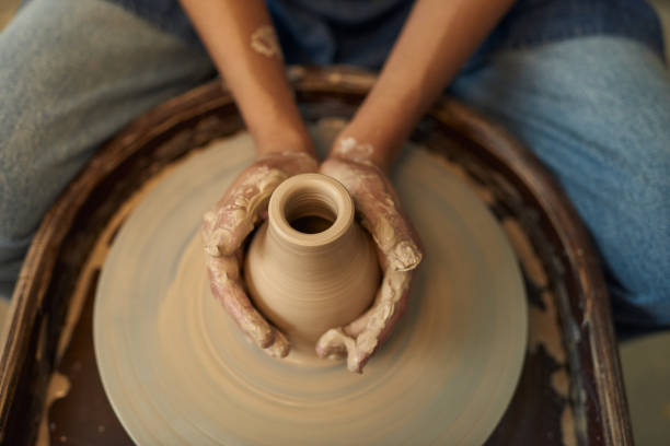 istock Hands of young artisan touching clay jug during work by pottery wheel 1353393652