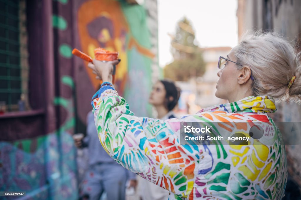 Female street artists Three women, young females street artists looking together on a building wall drawing outdoors. Street Artist Stock Photo
