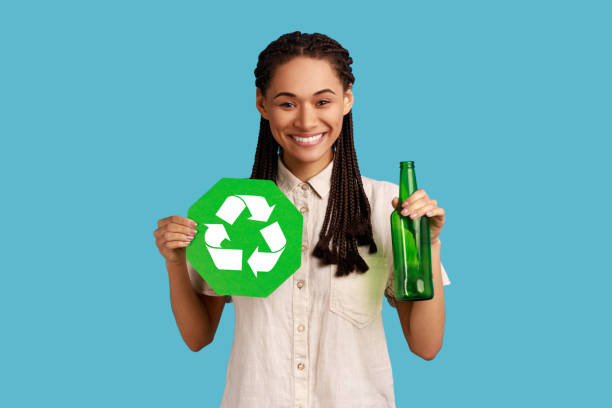 mujer con rastas mirando a la cámara con una sonrisa dentada, sosteniendo un letrero de reciclaje y una botella de vidrio. - recycling recycling symbol environmentalist people fotografías e imágenes de stock