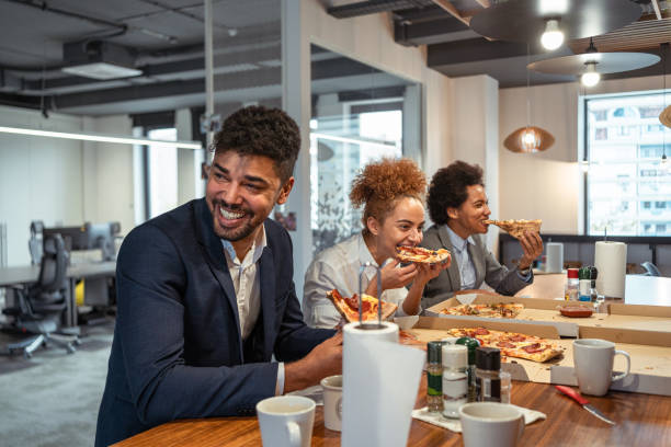 Multiracial group of business people, eating a pizza for their lunch break at cafeteria stock photo
