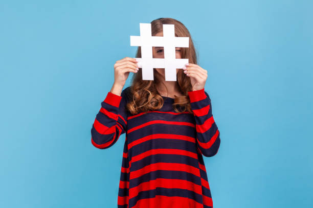istock Woman looking at camera through large white hashtag symbol with prying eye, interesting web content. 1353399072
