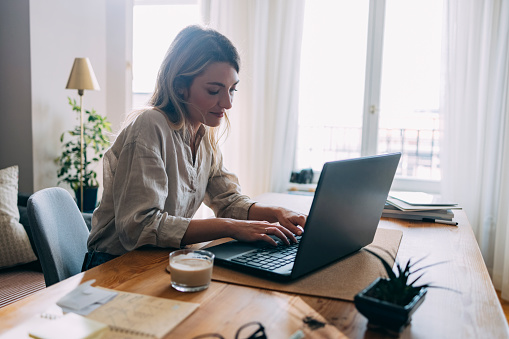 Beautiful businesswoman typing something on laptop keyboard while sitting at home office desk