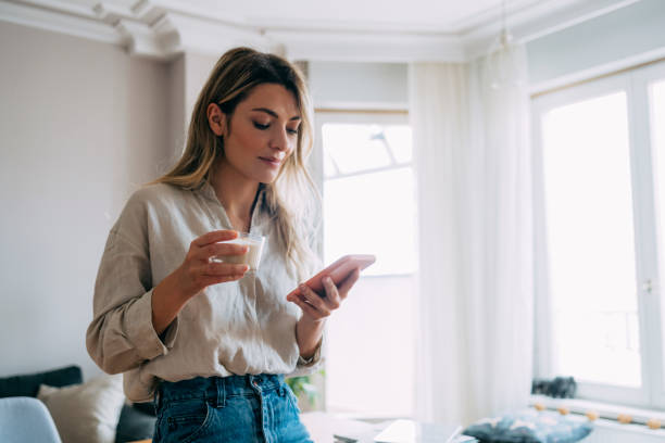 istock Happy Woman Drinking Coffee and Using Mobile Phone at Home 1353399730