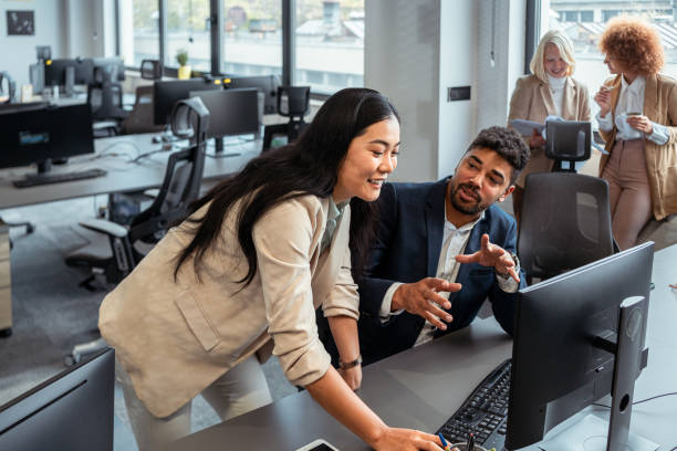 Mixed-race businessman, having a casual conversation with the female CEO of Asian ethnicity, while she helping him about work on computer stock photo
