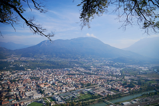 View of buildings and the Cathedral Tower in a sunny day in Trento city centre. Dolomites in background; Trentino-Alto Adige, Italy