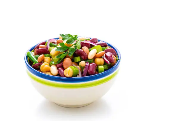 Healthy eating and vegan food: close up view of a single bowl of fresh healthy bean salad isolated on white background. The composition is at the left of an horizontal frame leaving useful copy space for text and/or logo at the right. High resolution 42Mp studio digital capture taken with Sony A7rII and Sony FE 90mm f2.8 macro G OSS lens