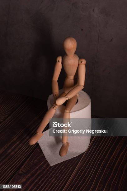 A Wooden Man Is Sitting On A Roll Of Toilet Paper In A Dark Room The Doll Is Experiencing Stomach Problems And Intestinal Diseases Stock Photo - Download Image Now