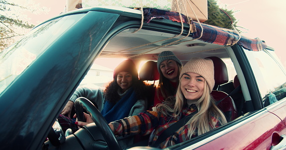 Tres jóvenes felices mujeres multiétnicas emocionadas posando, sonriendo a la cámara en un elegante automóvil rojo en la carretera nevada de invierno a cámara lenta. photo