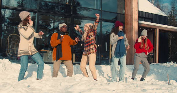 WINTER VACATION. Group of happy fun multiethnic young friends dance together at sunny snowy house terrace slow motion.