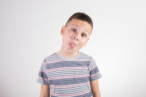 Portrait of funny naughty little boy in T-shirt sticking out tongue, white background