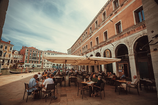 Venice, Italy:  People having dinner at street cafe in historical area near canal on 29 September 2021. Ancient italian city and lagoon are UNESCO World Heritage Sites