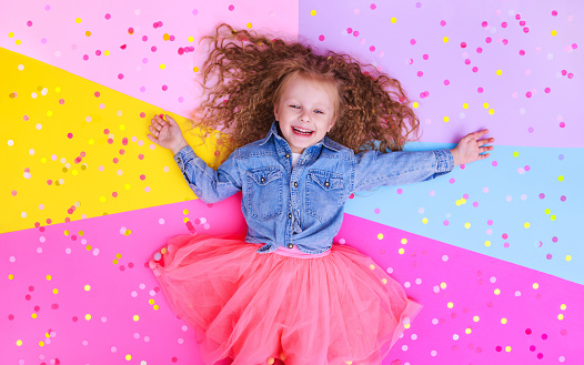 little girl laughs rejoices on a blue background with confetti top view birthday celebration concept