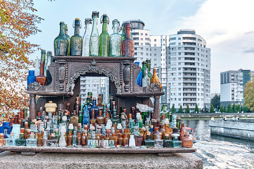 Kaliningrad, Russia - September 11. 2021: Antique colored various bottles and phials from under drinks, medicines or perfume on carved wooden shelf as souvenirs for tourists over backdrop of cityscape