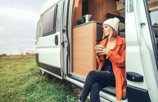 woman drinking coffee sitting at the door of a campervan - rv bildbanksfoton och bilder
