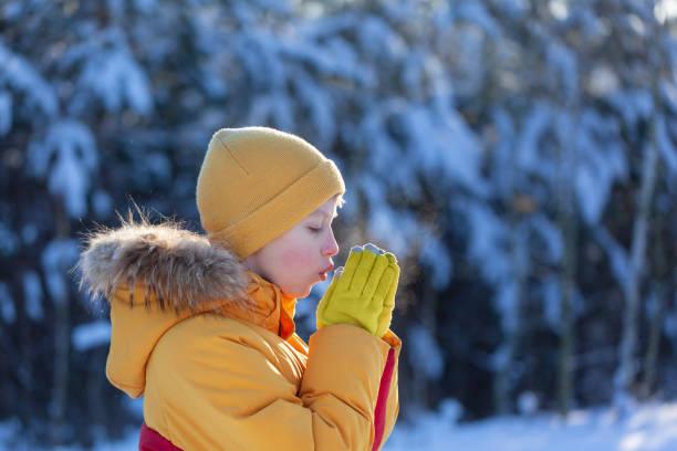 Portrait of a kid boy outdoors in warm clothes and mittens warms his hands with his breath. stock photo