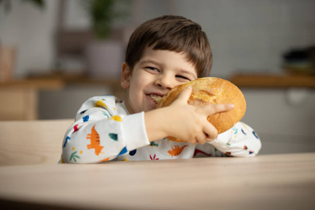 istock Adorable little boy eating bread in the kitchen . 1353418915