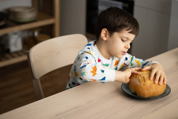 istock Adorable little boy eating bread in the kitchen . 1353418917