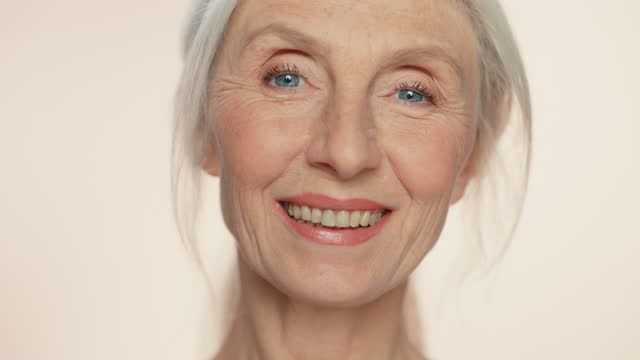 Close-up Portrait of Beautiful Senior Woman Turning around, Looking at Camera and Smiling Wonderfully. Elderly Beauty. Graceful of Old Age Concept for Skincare, Cosmetics Product. Gradual Focus