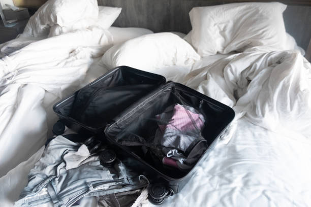 istock Open suitcase with clothing on messy white bed in the hotel. 1353422426
