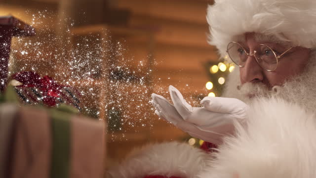 Santa Claus creates magic.Closeup portrait of Santa Claus blowing snow out of hands, slow motion. magic Christmas atmosphere, glowing effect.