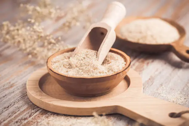 Photo of Heap of psyllium husk in wooden bowl on wooden table table