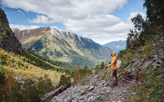 travel to Caucasus mountains in Karachay-Cherkessia, Arkhyz. Man in yellow hipster hoodie hiking in mountains with travel backpack. Wandering lifestyle, adventure concept autumn vacation in wild