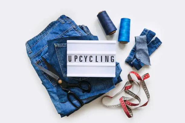 Denim Upcycling Ideas, Using Old Jeans, Repurposing Jeans, Reusing Old Jeans, Upcycle Stuff. Lightbox with text Upcycling, Stack of old blue jeans, scissors, thread and sewing tools in sewing studio