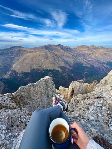 A female hiker resting in the sunshine and taking in the views from the mountain summit of Meall Corranaich in the Scottish Highlands, UK landscape.