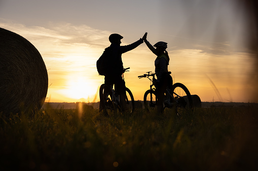Silhouette of couple on bicycle giving high five on field during sunset